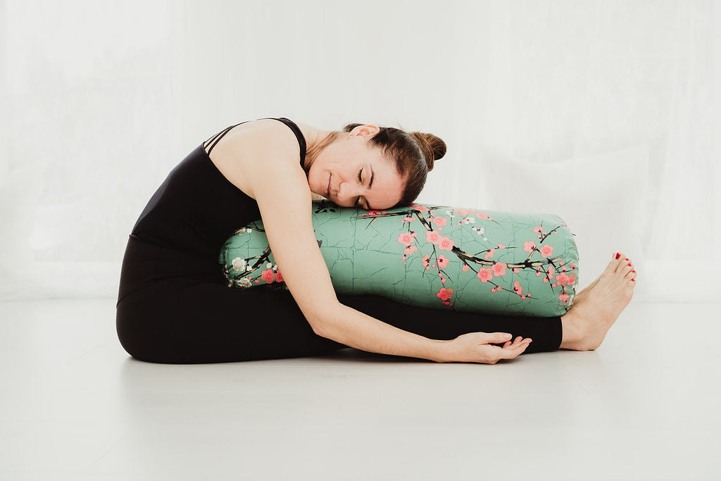 Eine Frau übt Yoga Vorbeugen im Sitzen mit einem Yogabolster in einem hellen Raum.