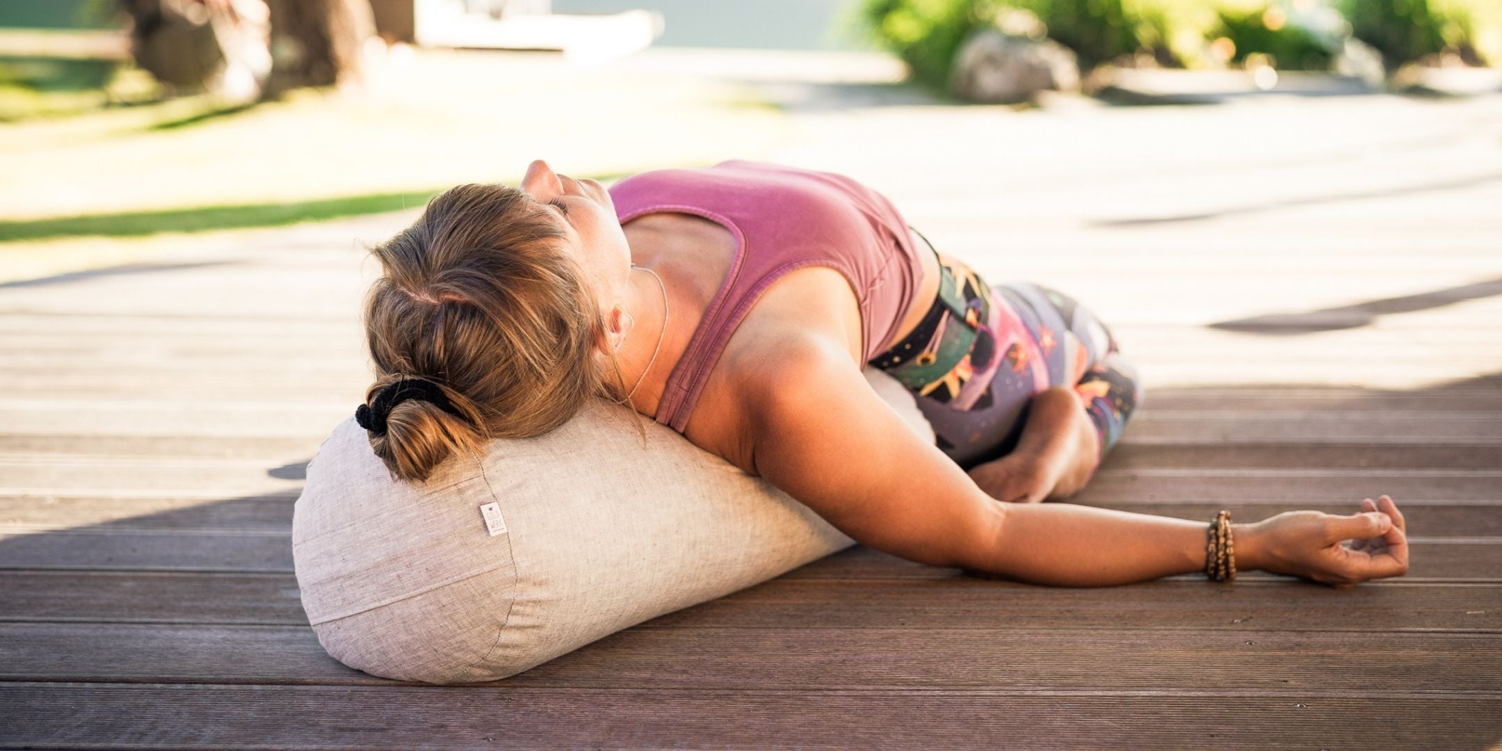 Frau übt die Yin Yoga Haltung "Sattel" mit einem Yogabolster in der Natur.