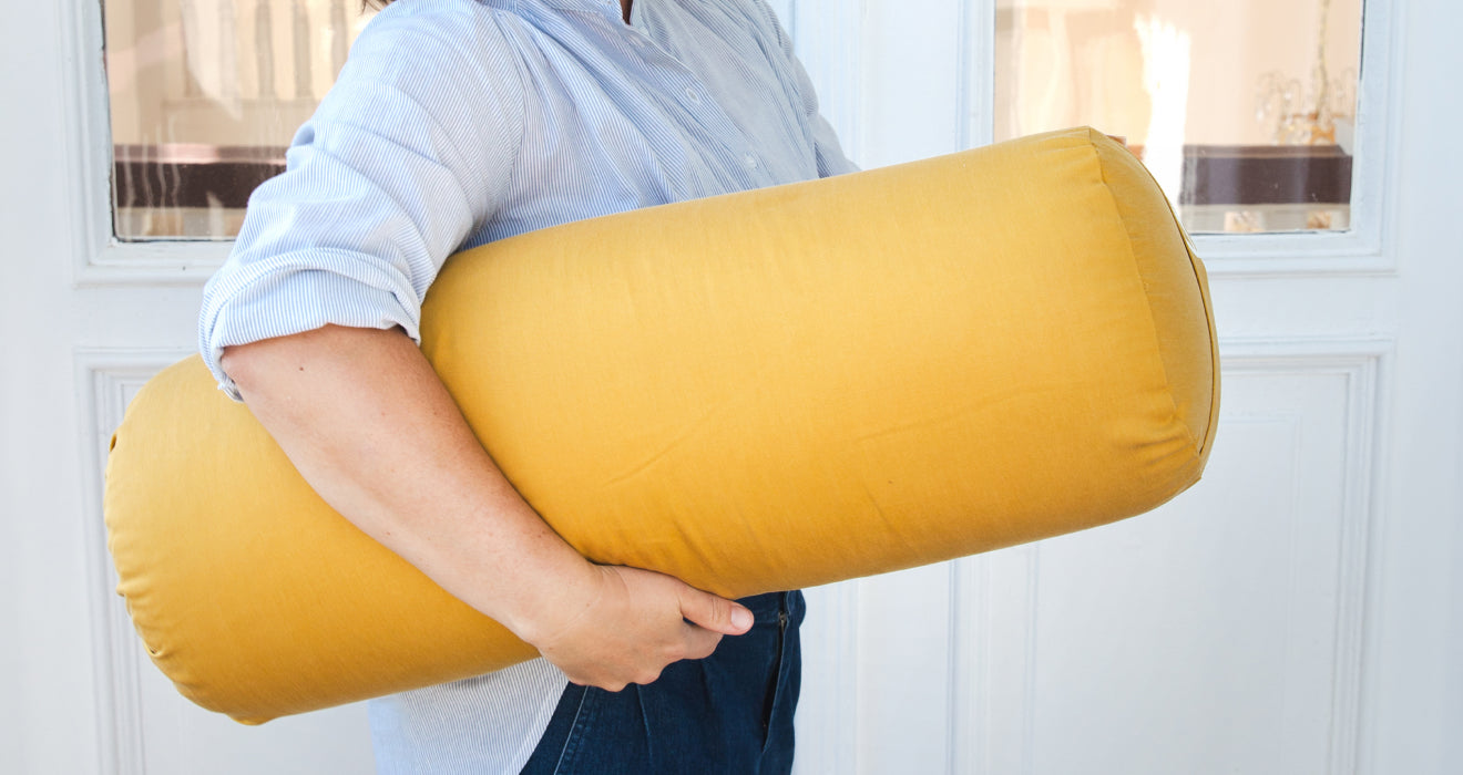 Eine Frau trägt ein gelbes Yoga Bolster unter ihrem Arm.