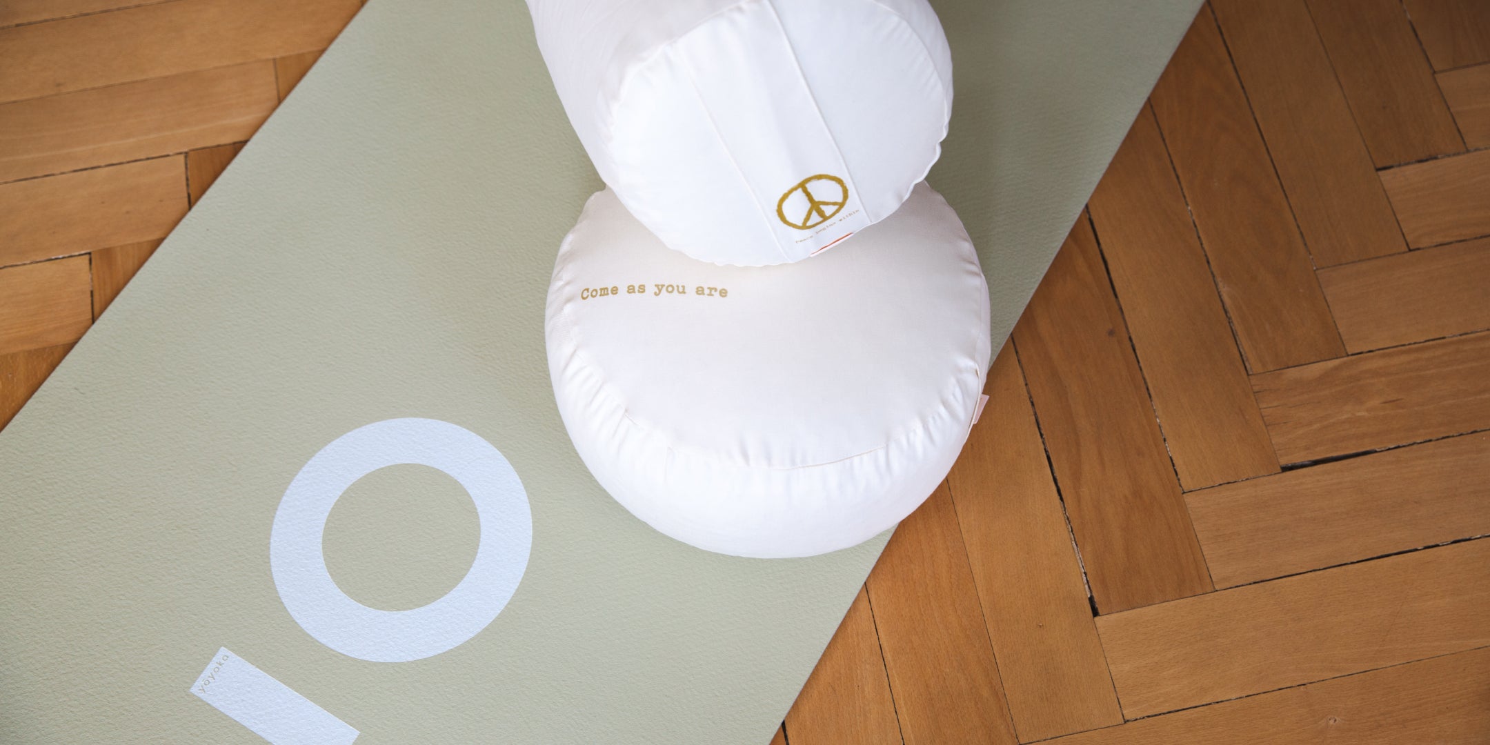 Auf einer Yogamatte liegen ein Meditationskissen und ein Yoga Bolster.