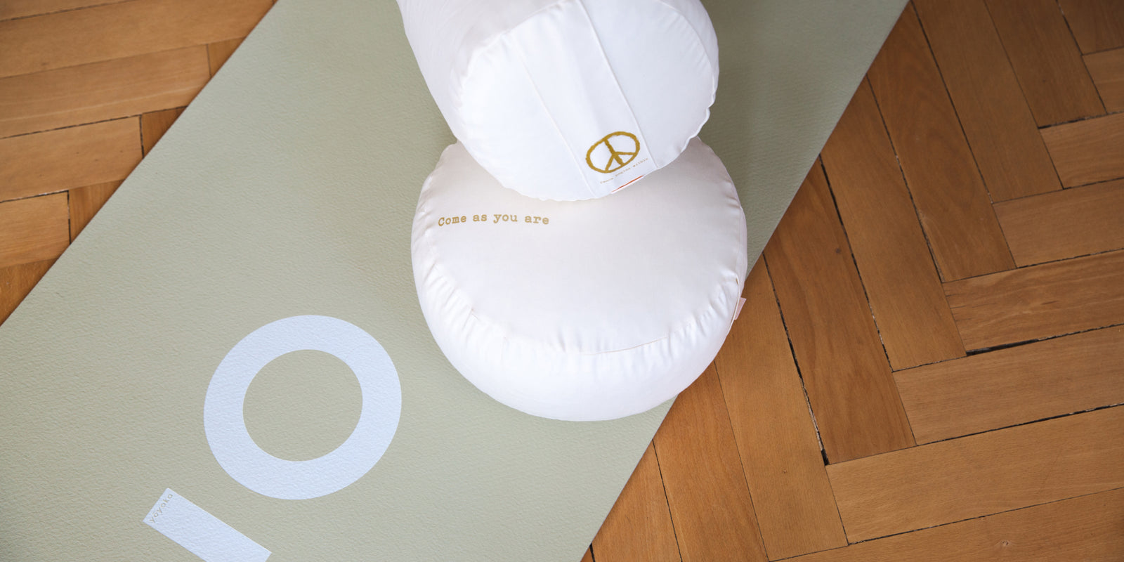 Auf einer Yogamatte liegen ein Meditationskissen und ein Yoga Bolster.