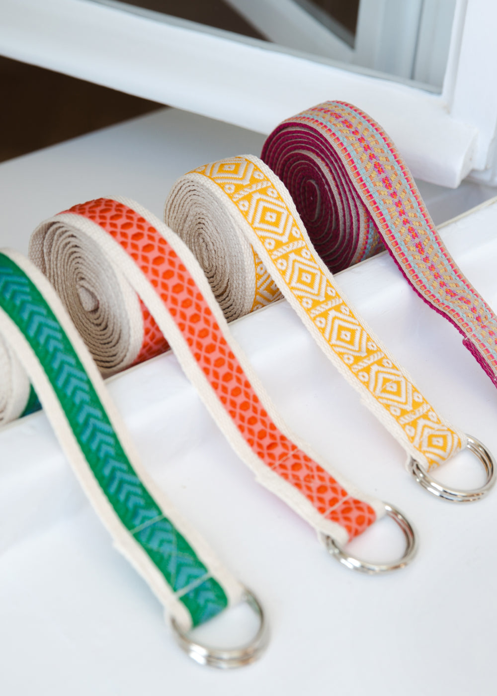 Vier verschiedene Yogagurte liegen in einem weißen Fensterrahmen.