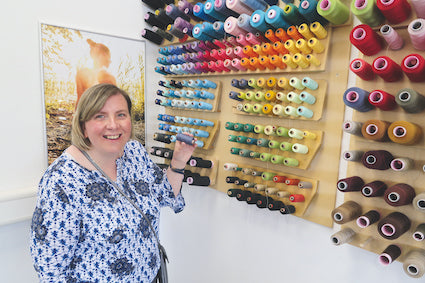 Eine lachende Frau neben einem Brett voller bunter Nähgarne.