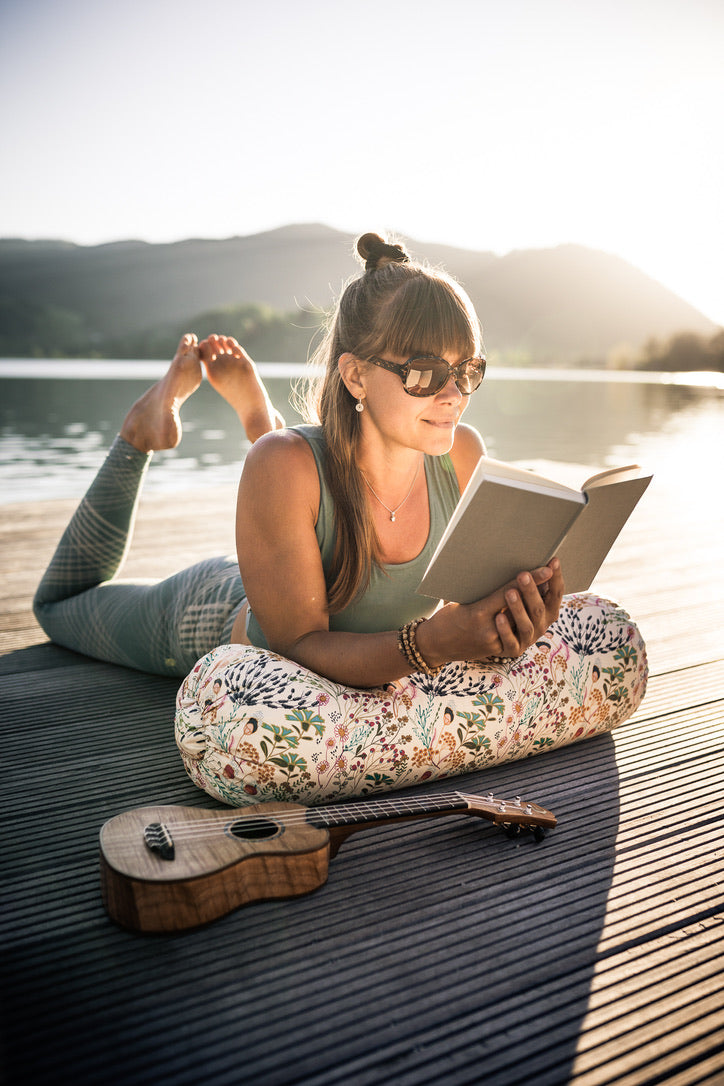 Frau liegt im Sommer auf einem Steg und liest. Ihre Arme stützen sich dabei auf eine Yogabolster.