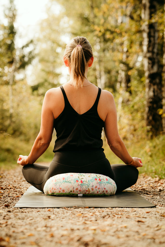 Eine meditierende Frau von hinten in einem lichten Wald.