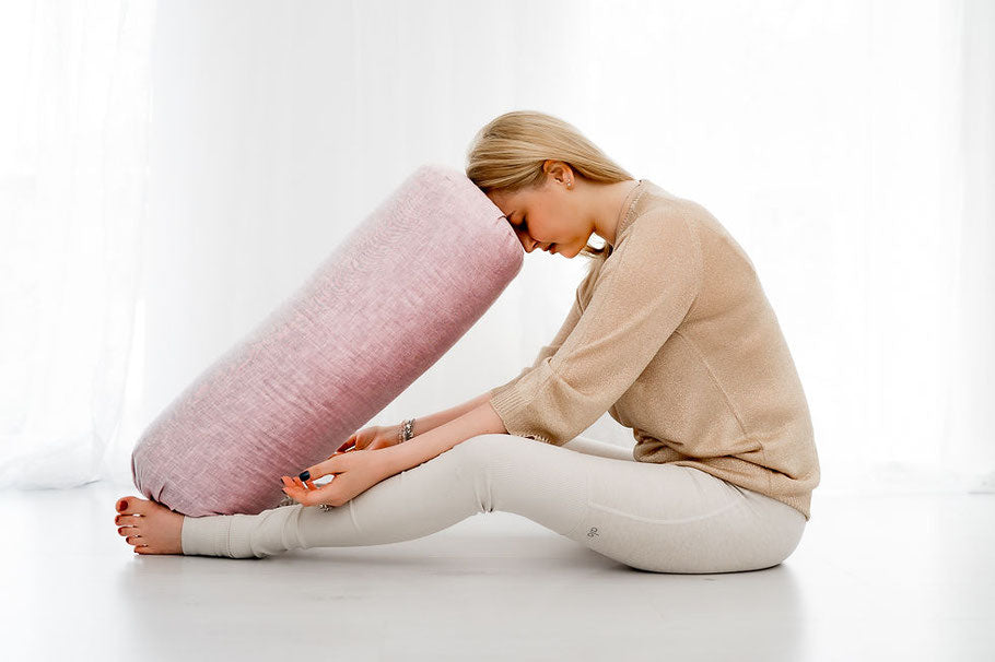 Eine Frau übt eine Vorbeuge im Sitzen und stütz dabei ihre Stirn auf ein Yogabolster.