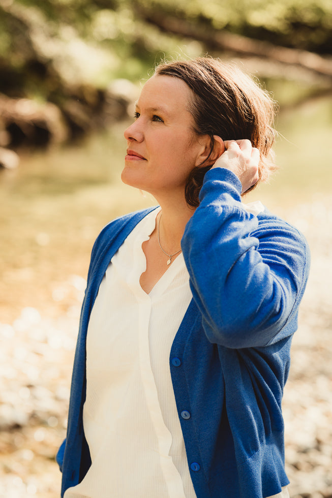 Frau mit blauer Strickjacke und weißem Hemd streicht sich Haare hinter das linke Ohr.