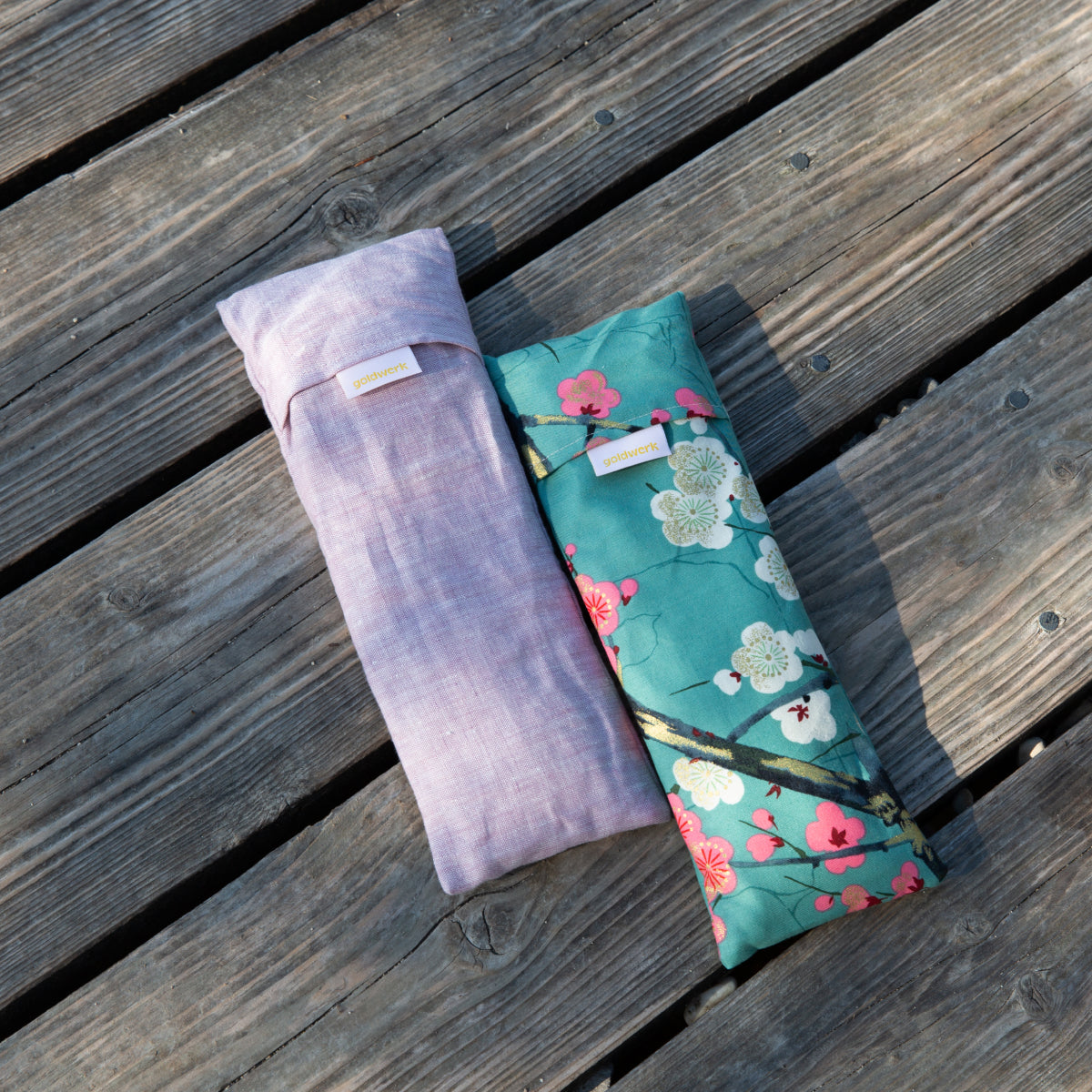 Zwei Augenkissen in rosa und bunt liegen auf einem Holzsteg.