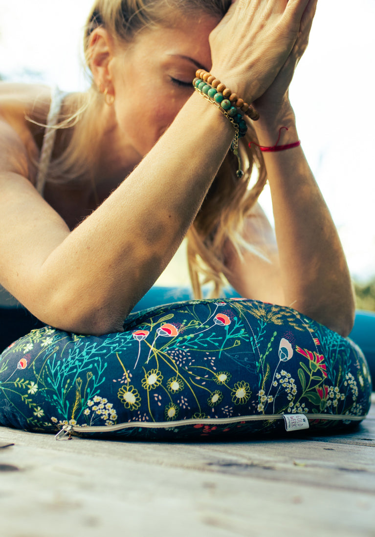 Eine Frau übt Yoga und praktiziert gerade eine Vorbeuge mit Hilfe eines Yoga Halbmondkissens.