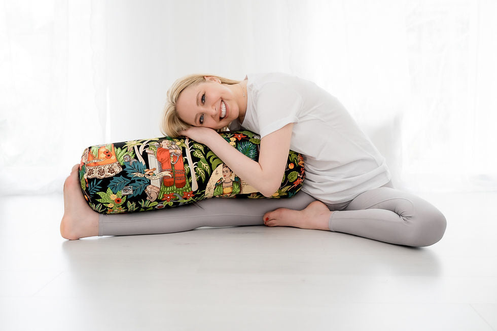 Eine Frau übt Seitbeugen in einem hellen Raum mit einem bunten Yogabolster.