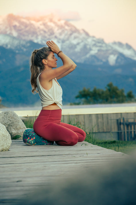 Frau meditiert auf einem grünen Meditationskissen vor einem Alpenpanorama