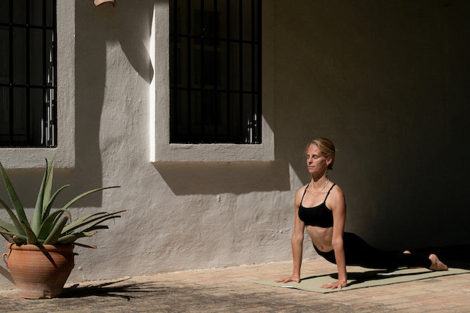 Eine junge Frau übt Yoga vor einer weißen Hauswand