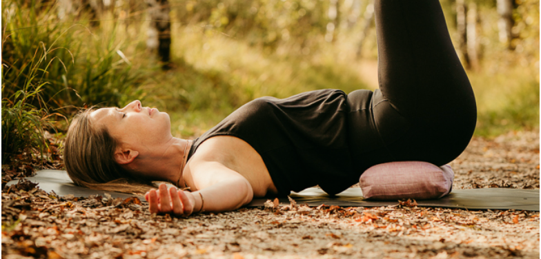 Eine Frau übt Yin Yoga mit einem Lagerungskissen in der Natur und hat ihre Augen geschlossen.